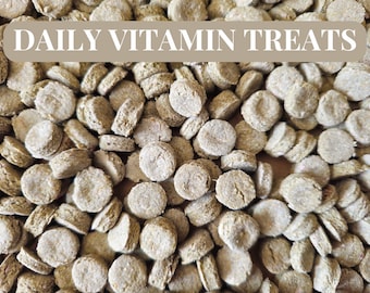 May include: A close-up image of a pile of small, round, light brown dog treats. The treats are labeled "DAILY VITAMIN TREATS".