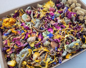 May include: A close-up of a mix of dried flowers, petals, and herbs in a cardboard box. The mix includes yellow, orange, pink, purple, and blue flowers.