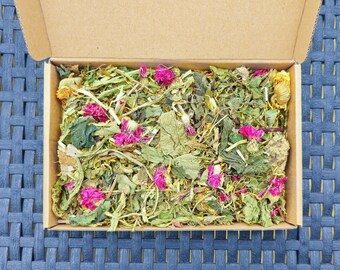 May include: A cardboard box filled with a variety of dried herbs and flowers, including pink and yellow blossoms.