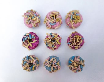 May include: Nine mini donuts with pink and blue frosting and colorful sprinkles.