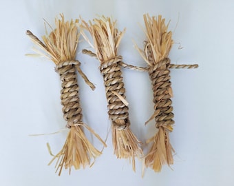 May include: Three brown straw bundles tied together with a brown twine. The bundles are made of natural straw and have a rustic look.