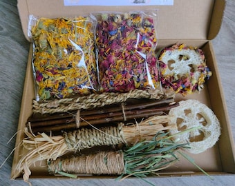 May include: A box filled with natural materials for small animal enrichment. It includes dried flowers, dried herbs, woven rope, sticks, and loofah.