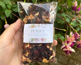 May include: A clear plastic bag filled with a blend of dried fruit and berries. The bag has a white label with the text "PURIFY A SPECIALISED TREAT MIX FILLED WITH VITAMINS, ANTIOXIDANTS AND MORE. 50g".