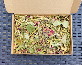 May include: A cardboard box filled with a blend of dried herbs and rose petals. The herbs are a mix of green and brown, with some yellow and pink petals visible.