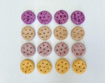 May include: A set of 18 round dog treats in three colors: purple, brown, and yellow. The treats are arranged in three rows of six.
