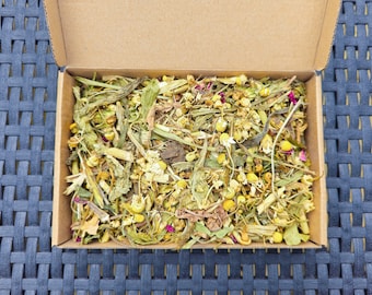 May include: A cardboard box filled with a blend of dried herbs and flowers, including chamomile, lavender, and rose petals. The herbs are a light green and yellow color, while the petals are a deep pink.