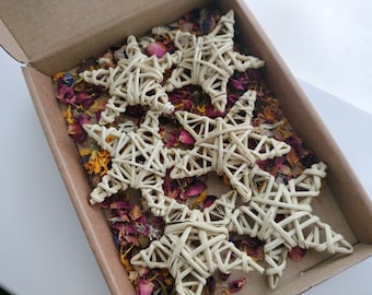 May include: A set of five woven wicker star ornaments in a cardboard box with dried flower petals. The stars are a light beige color and are arranged in a random pattern.
