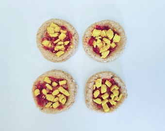 May include: Four round cookies with a red filling and yellow sprinkles on top.