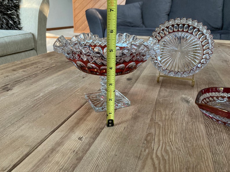 Puede incluir: Un juego de tres cuencos de vidrio transparente con un patr&oacute;n rojo en forma de diamante. Los cuencos est&aacute;n sobre una mesa de madera.