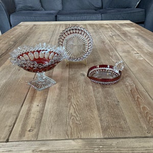 Puede incluir: Tres cuencos de vidrio con un dise&ntilde;o de vidrio cortado. Los cuencos est&aacute;n sobre una mesa de madera. Los cuencos son rojos y transparentes.
