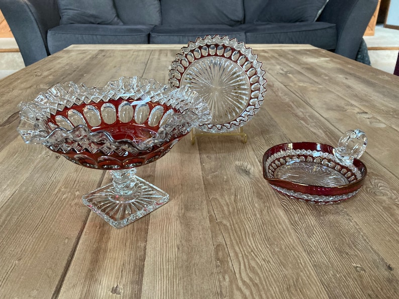 Puede incluir: Tres cuencos de vidrio transparente con un tinte rojo rub&iacute;. Los cuencos tienen un borde festoneado y un patr&oacute;n decorativo. Los cuencos est&aacute;n sobre una superficie de madera.