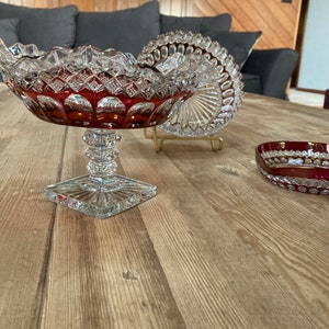 Puede incluir: Tres cuencos de vidrio vintage de color rojo rub&iacute; y detalles en vidrio transparente. Los cuencos est&aacute;n sobre una superficie de madera.