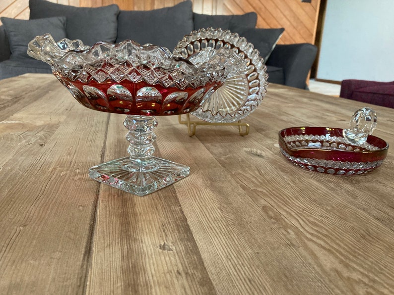 Puede incluir: Tres cuencos de vidrio vintage de color rojo rub&iacute; y detalles en vidrio transparente. Los cuencos est&aacute;n sobre una superficie de madera.
