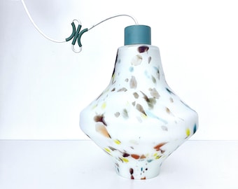 May include: A white pendant light fixture with a speckled design in various colors, including brown, yellow, and blue. The light has a teal-colored top and a matching teal-colored ceiling mount. The fixture hangs from a white cord.