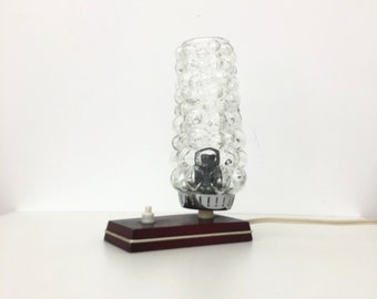 May include: A vintage table lamp with a clear glass shade featuring a bubbled texture. The lamp has a dark wood base with a white switch.