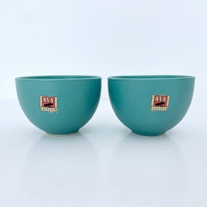 May include: Two teal blue ceramic bowls with a red and white logo that says "AIA PROVENCE" on each bowl.