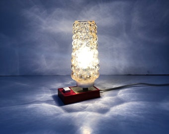 May include: A small table lamp with a clear glass shade with a bubbled texture. The lamp has a red base with a white switch.