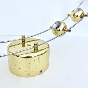 Könnte beinhalten: Eine Vintage-Schreibtischlampe aus Messing mit drei kugelförmigen Leuchten. Die Lampe hat einen zylindrischen Sockel und dünne, silberfarbene Arme, die die Leuchten tragen. Das Messing hat einen warmen, goldenen Farbton, und das Design ist elegant und modern.