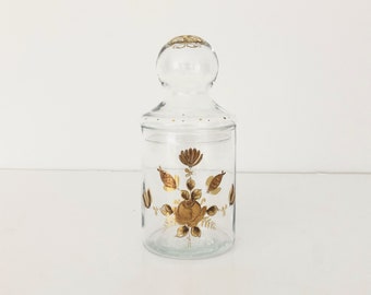 May include: A clear glass jar with a gold floral design. The jar has a lid with a knob on top.