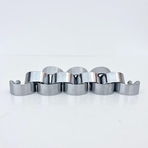 Peut inclure: Un bracelet en métal argenté avec un design unique et articulé. Le bracelet est composé d'une série de maillons cylindriques arrondis reliés par des segments plats et incurvés. Le métal poli reflète la lumière, créant un aspect brillant. Le bracelet est présenté sur une surface blanche.