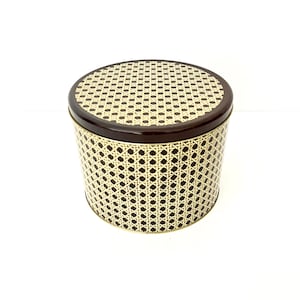 May include: A round, brown metal tin with a gold wicker pattern. The lid is closed.