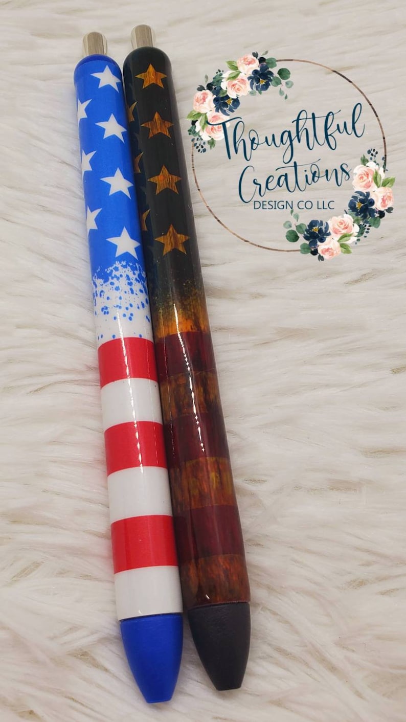 Pode incluir: Duas canetas com designs patri&oacute;ticos e detalhes prateados. Uma apresenta um design de estrelas azuis e brancas, a outra um design vermelho, branco e castanho. As canetas t&ecirc;m um acabamento brilhante e pontas azuis e pretas. Medem cerca de 15 cm.