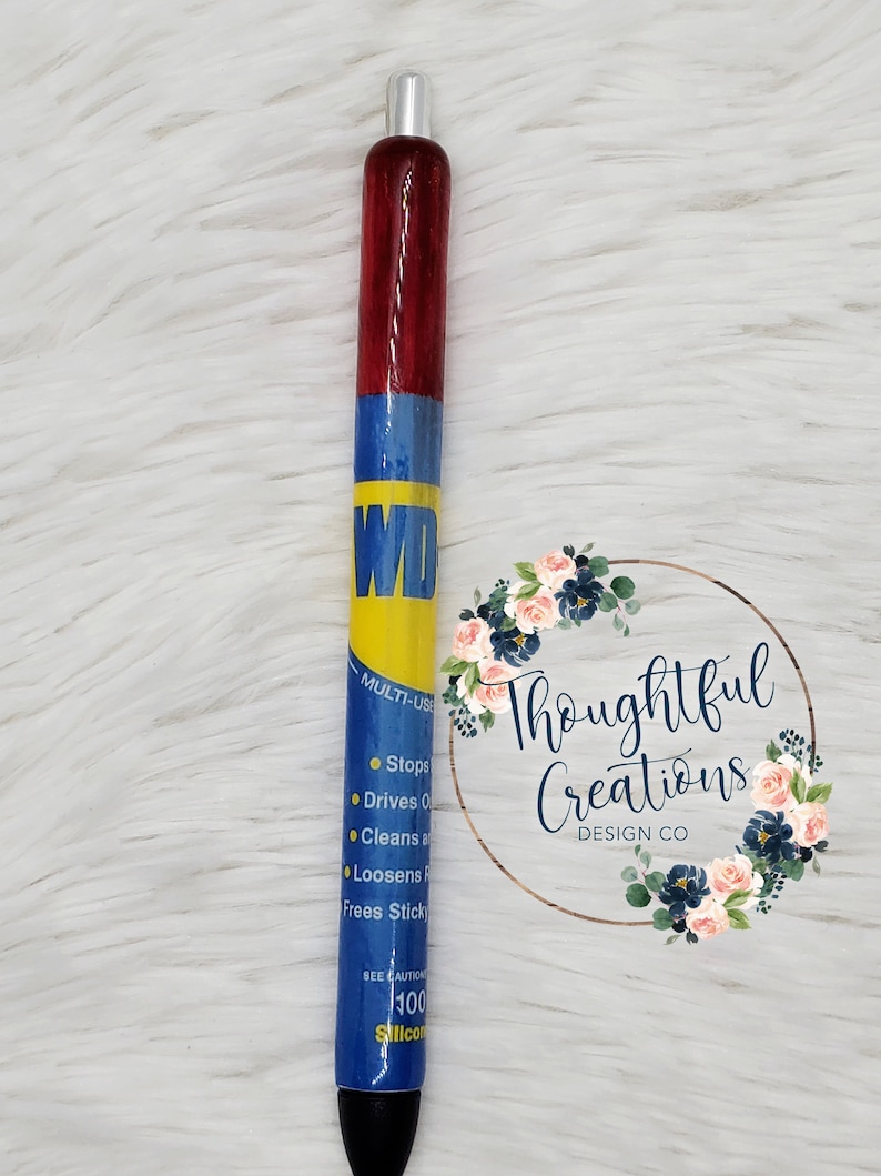Pode incluir: Uma caneta personalizada com um design vermelho, azul e amarelo, com o texto "WD" e informa&ccedil;&otilde;es sobre o produto. A caneta tem uma ponta prateada e uma base preta. &Eacute; um instrumento de escrita &uacute;nico e feito &agrave; m&atilde;o.