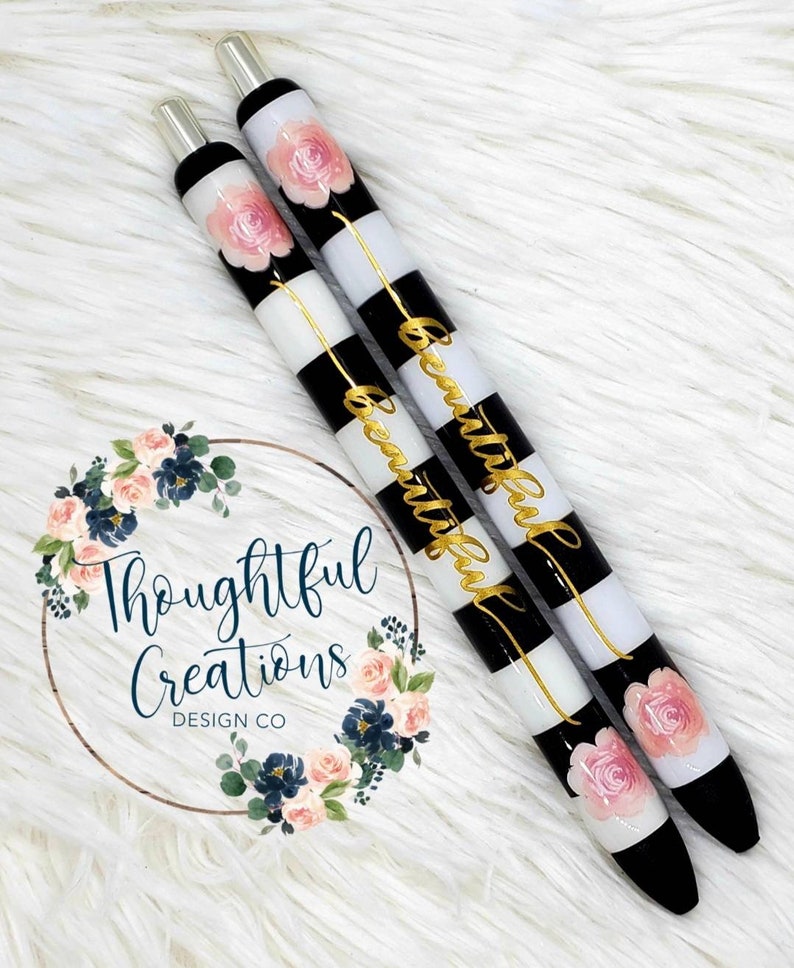 Pode incluir: Duas canetas com listras pretas e brancas e a palavra "Beautiful" em letras douradas. Cada caneta tem um desenho de rosa rosa e detalhes em preto e prata. As canetas s&atilde;o da Thoughtful Creations Design Co.