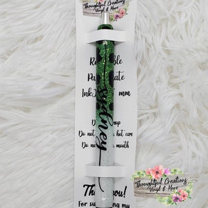 May include: A handmade pen with a green glitter leopard print design and the name "Sydney" in cursive. The pen is packaged with a white card that includes the text "Hand Made By Thoughtful Creations Vinyl & More."