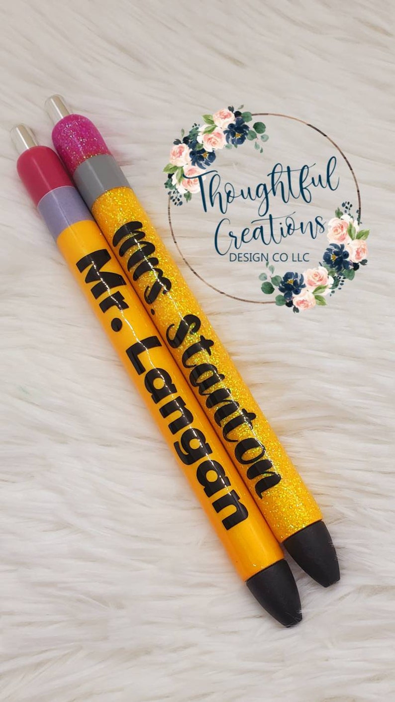 Pode incluir: Duas canetas personalizadas com detalhes de glitter. Uma caneta &eacute; amarela com "Mr. Langan" em preto, a outra &eacute; amarela com "Mrs. Stanton" em preto. Ambas as canetas t&ecirc;m pontas pretas e tampas prateadas. As canetas est&atilde;o sobre uma superf&iacute;cie branca e fofa.