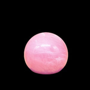 Pode incluir: Uma esfera lisa de cor rosa feita de quartzo rosa. A esfera tem um tom rosa claro com sutis veios brancos.