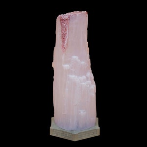 May include: A large, pink selenite crystal with a hexagonal base. The crystal has a rough, textured surface and a reddish-brown streak running down the side.