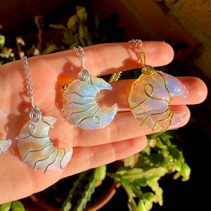 Può includere: Tre ciondoli di cristallo iridescente a forma di luna avvolti in filo d'oro e d'argento, appesi a delicate catene. I ciondoli sono esposti su una mano su uno sfondo di pianta verde.