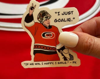 Puede incluir: Una pegatina con un portero de hockey de dibujos animados haciendo un signo de paz, vistiendo una camiseta roja, negra y blanca con un logotipo de equipo. El texto en la pegatina dice "I just goalie." y "If we win, I happy, I smile. - PK"