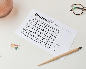 May include: A white Bunco score sheet with a grid for tracking game scores. The sheet includes the word "Bunco" at the top, dice icons, and spaces for names, bonuses, wins, and losses. A wooden pen and eyeglasses are also on the white surface.