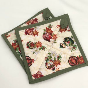 May include: Two green quilted pot holders with a cream background and a Christmas ornament pattern. The ornaments are red, green, and gold with white accents.