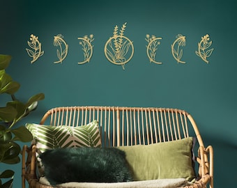 May include: A set of seven gold metal wall decor pieces in the shape of crescent moons with floral designs. The decor is displayed on a teal wall above a light brown wicker couch with green and white patterned pillows.