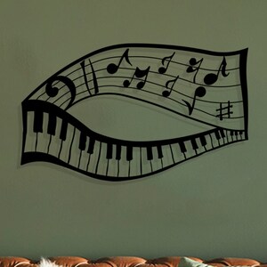 May include: Black metal wall art featuring a musical note staff with piano keys and musical notes. The art is displayed on a green wall above a brown leather sofa with pillows.