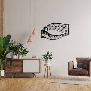 May include: Black metal wall art depicting a musical staff with notes and a piano keyboard. The art is mounted on a white wall above a wooden cabinet with a white door. There are two pink pendant lights hanging from the ceiling.