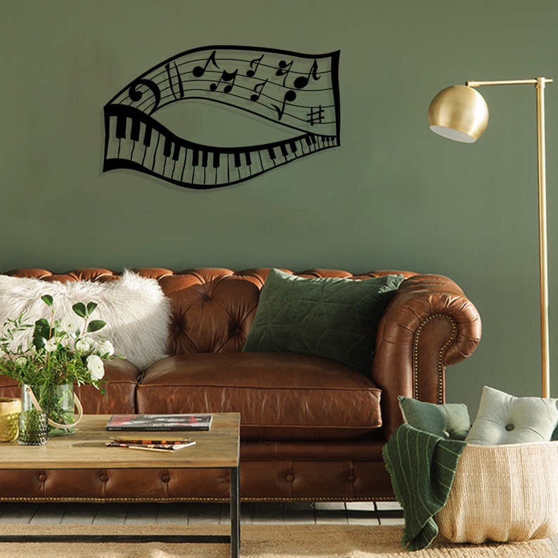 May include: Black metal wall art featuring a musical note staff with piano keys and musical notes. The art is displayed on a green wall above a brown leather sofa with pillows.