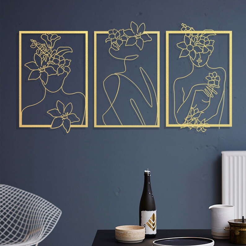 Pu&ograve; includere: Tre pezzi di arte da parete in metallo dorato con un disegno a linea di un viso di donna con fiori tra i capelli. Il corpo della donna &egrave; anche disegnato in uno stile di arte lineare.