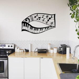 May include: Black metal wall art featuring a musical note design with a piano keyboard. The art is mounted on a white wall above a kitchen counter with a stainless steel stove and white cabinets.