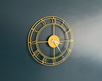 May include: A gold-colored metal wall clock with Roman numeral markings and a white face. The clock has a simple design with four arms and a small center circle.