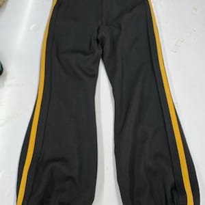 May include: Black pants with a yellow stripe down each side. The pants have a flared leg design and a black elastic cuff at the ankle. The pants are made of a smooth, possibly athletic, material.