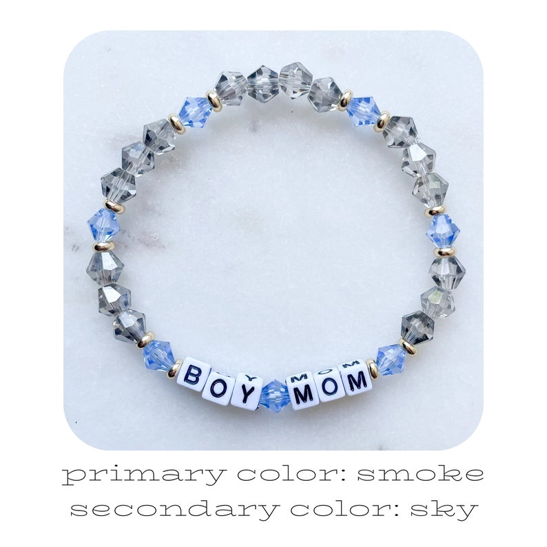 May include: A beaded bracelet with alternating smoke and sky blue crystals. The bracelet has the words "BOY MOM" spelled out in white letters on black squares.