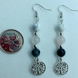 May include: Silver earrings with a tree of life charm, featuring white, pink, and grey beads.