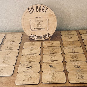 May include: A wooden game for a baby shower or gender reveal party. The game is called "Oh Baby, I am the size of a Pumpkin, Watch Me Grow!" and features 24 wooden cards with different fruits and vegetables printed on them.
