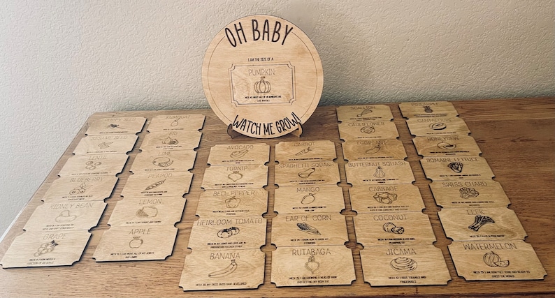 May include: A wooden game for a baby shower or gender reveal party. The game is called "Oh Baby, I am the size of a Pumpkin, Watch Me Grow!" and features 24 wooden cards with different fruits and vegetables printed on them.