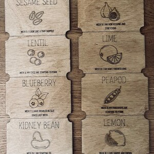 May include: A set of 10 wooden cards with illustrations of different fruits and vegetables at various stages of growth. Each card features the name of the fruit or vegetable, a simple illustration, and a description of its development during a specific week. For example, one card shows a blueberry and states "Week 7: I have doubled in size since last week."