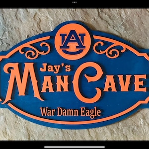 May include: A blue and orange wooden sign with the text "Jay's Man Cave" and "War Damn Eagle". The sign has an Auburn University logo at the top.
